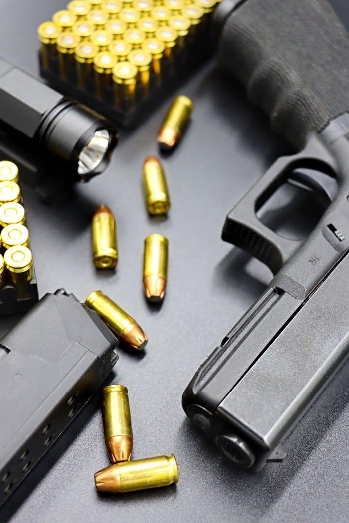 Detailed view of a black handgun with bullets and ammo clips on a black surface, showcasing firearm elements.
