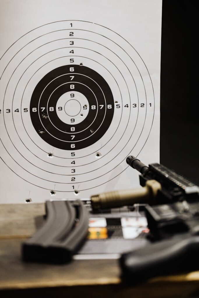 pexels-photo-5202428 Close-up of a rifle resting on a wooden surface with a target paper in the background.