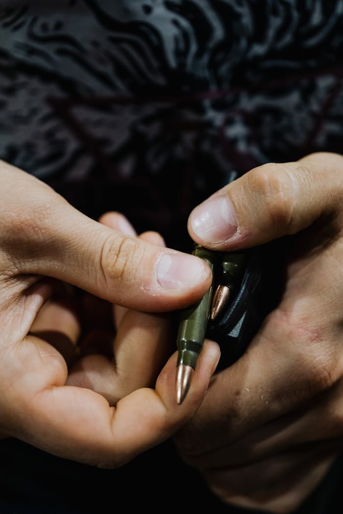 Detailed close-up of hands loading bullets into a rifle magazine.